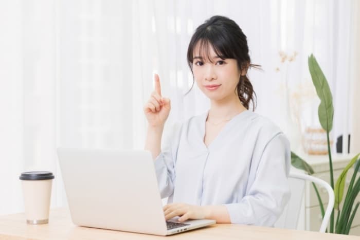 パソコンの前で指を立てる女性